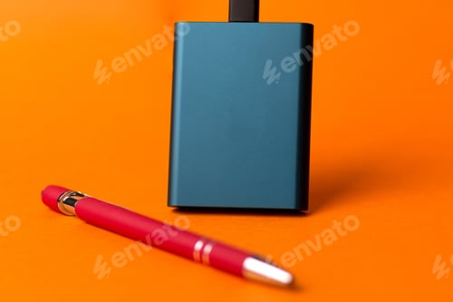Preview: External SSD disk and a red pen isolated on an orange background