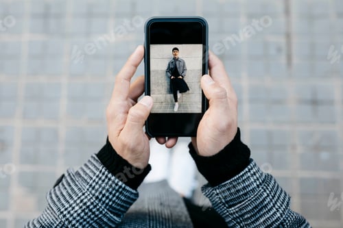 Preview: Man holding smartphone with photo of himself, close-up