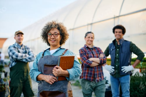 Preview: Happy greenhouse owner and group of her workers looking at camera.