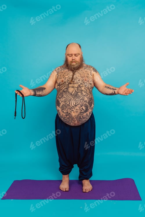 Preview: Hipster man with tattoos doing yoga and meditation exercises in the morning