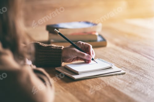 Preview: Closeup image of a woman writing on blank notebook on wooden table