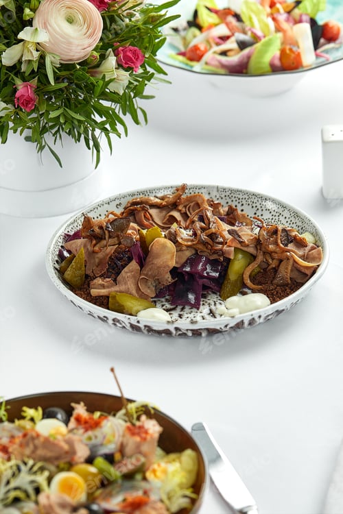 Preview: Sliced boiled beef tongue on a plate with fresh herbs and pickled cucumbers, light background