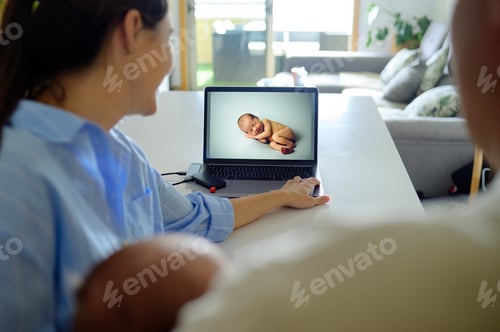 Preview: Crop family watching photos of newborn on computer with memory d