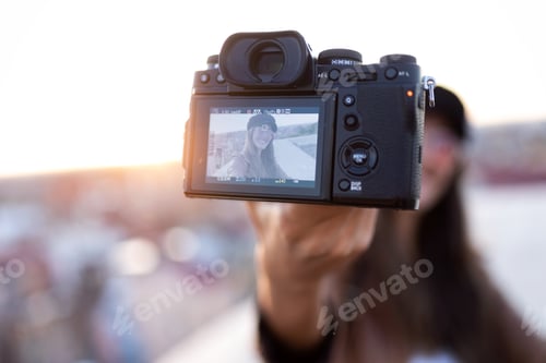 Preview: Pretty young woman taking a selfie with camera while sitting on the rooftop.