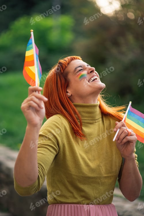Preview: Young woman holding rainbow flags and celebrating lgbtq plus pride in a park