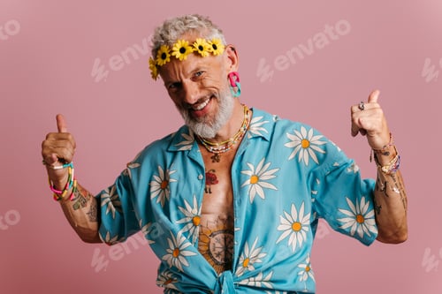 Preview: Cool senior man in stylish shirt and flower wreath on head standing against pink background