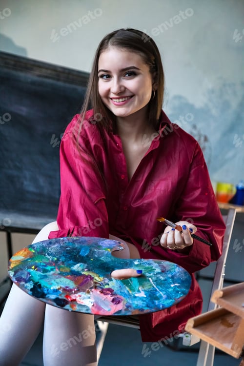 Preview: Pretty teen girl painter in red shirt painting at college art lab class, smiling looking