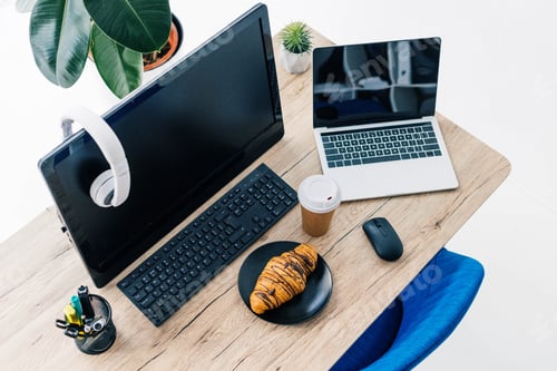 Preview: high angle view of headphones on blank computer monitor, laptop with blank screen, stationery,