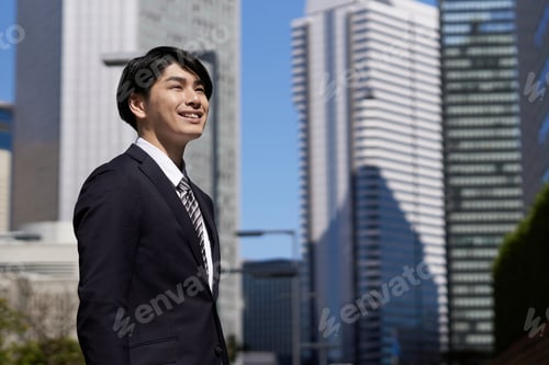 Preview: A smiling Japanese male businessman stands in an office district.