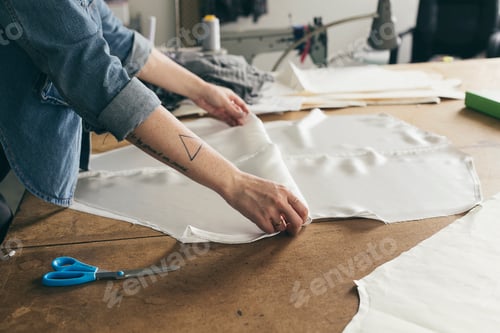 Preview: Young female seamstress folding pattern component in fashion studio