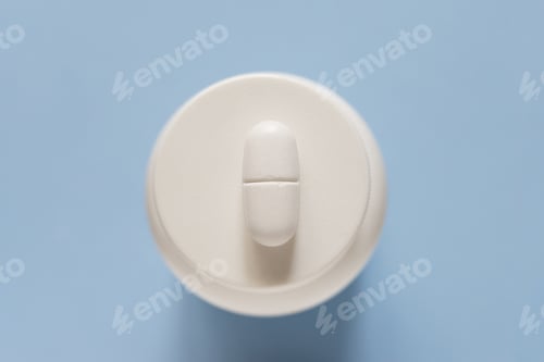 Preview: One large oblong pill lies on a jar of pills. Blue background.