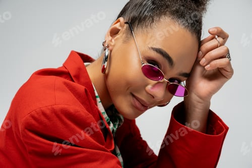 Preview: portrait of positive african american model in stylish attire and pink sunglasses on grey backdrop
