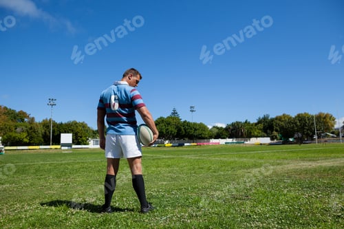 Preview: Rear view of rugby player holding ball at field