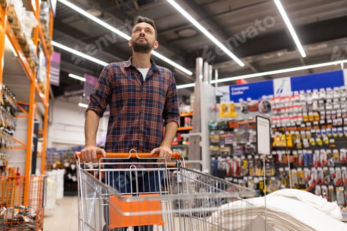 Preview: male shopper with a trolley oops examines racks with tools in a construction hypermarket