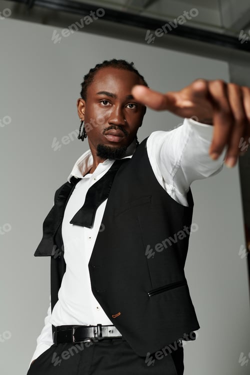 Preview: Confident young Black man in a stylish suit poses powerfully against a grey backdrop