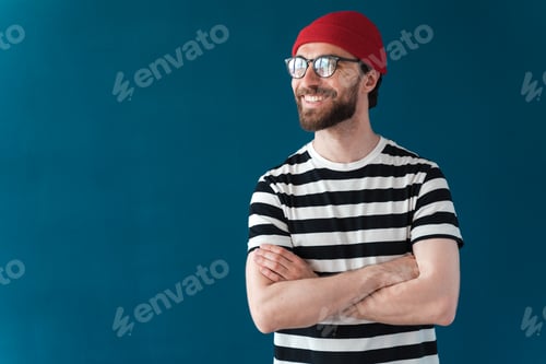 Preview: Smiling, positive guy with a beard and eyeglasses, red hat looks away. Attractive man