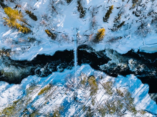 Preview: Aerial view of fast river with suspension foot bridge. Snow winter forest in Finland