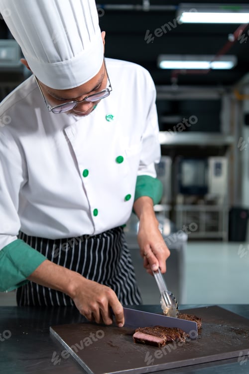 Preview: Young chef cutting medium-rare steak after it has been done grilling.