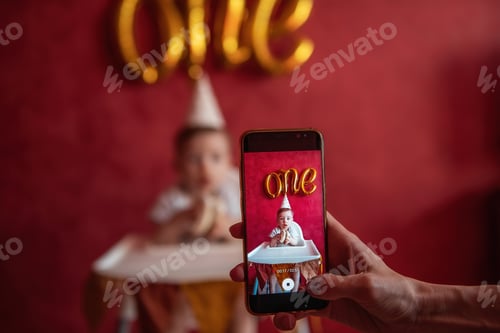 Preview: Mother uses smartphone to take pictures of one-year-old son, who is eating cake. Birthday at home