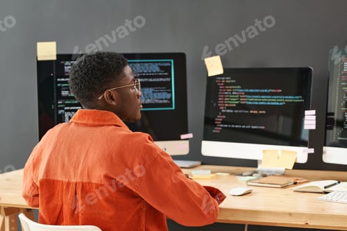 Preview: Rear view of young black man concentrating on decoding data on computer screen