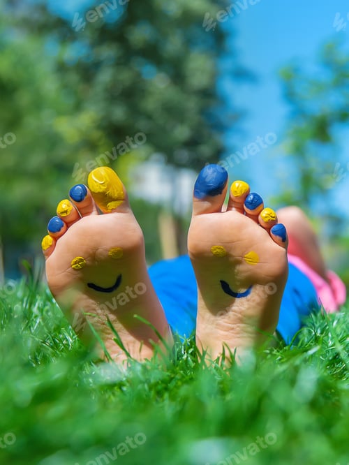 Preview: Child feet on the grass Ukrainian flag. Selective focus.