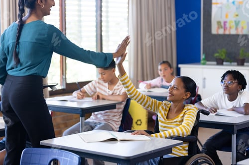 Preview: In school, Indian female teacher high-fiving student in wheelchair during classroom activity