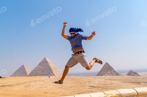 Preview: A young tourist jumping for joy in a blue turban and sunglasses at The Pyramids of Giza