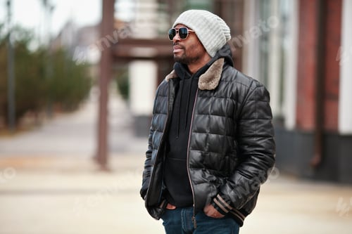Preview: Portrait of young handsome black man, standing on cityscape, looking away. Street style fashion