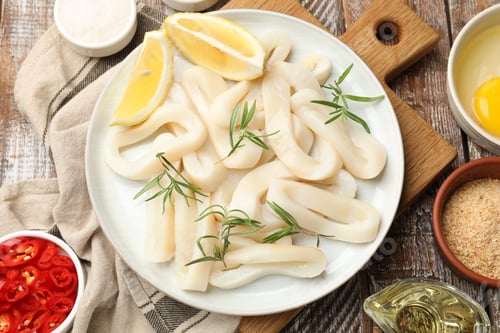 Preview: Uncooked squid rings, spices, yolk and bread crumbs on wooden table, flat lay