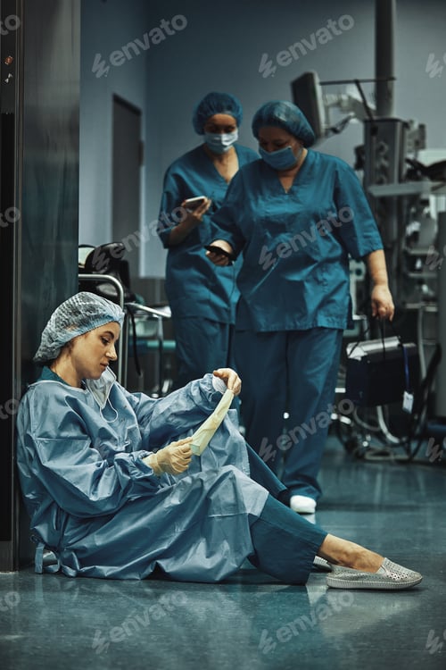 Preview: Tired doctor sitting after surgery in the hospital corridor. Great burden on doctors and medicine