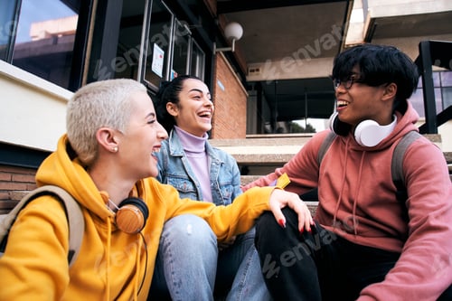 Preview: Group of three students laugh a lot sitting outdoors. Teenage gen z multiracial classmates are happy