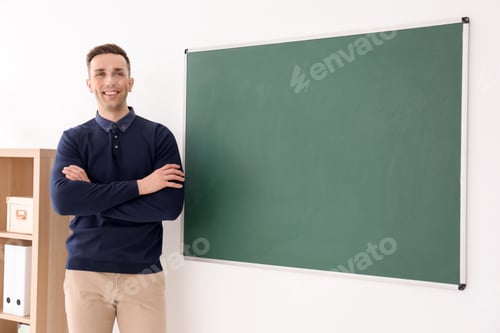 Preview: Young male teacher standing near blackboard in classroom
