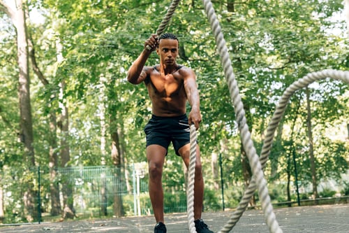 Preview: Man doing fitness workout with battling rope on sports ground