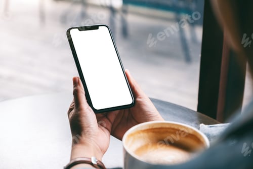 Preview: A woman holding black mobile phone with blank screen with coffee cup on wooden table