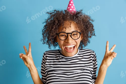 Preview: Cheerful woman in birthday cone hat doing victory gesture