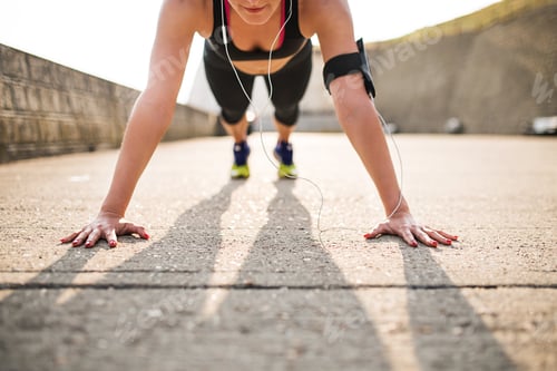 Preview: Young sporty woman runner with smartphone doing push-ups outside.