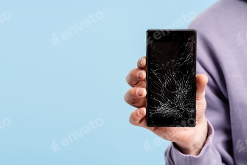 Preview: Hand holding smartphone with completely cracked and damaged screen showing repair need