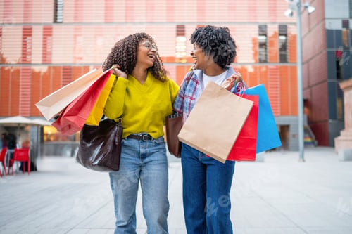 Preview: Two happy women shopping in city holding bags
