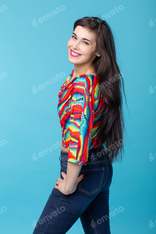 Preview: Cheerful young brunette woman with long hair posing on a blue background. The concept of a beautiful