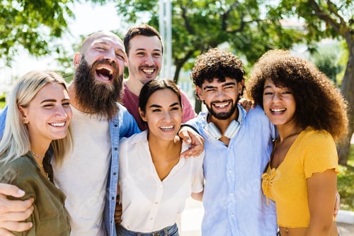 Preview: Portrait group of happy multiracial young friends hugging each other outdoors
