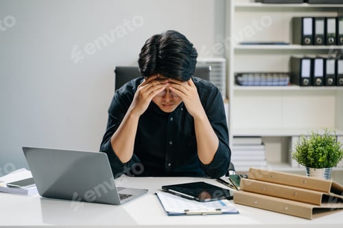 Preview: Frustrated young businessman working on a laptop computer sitting at his working place