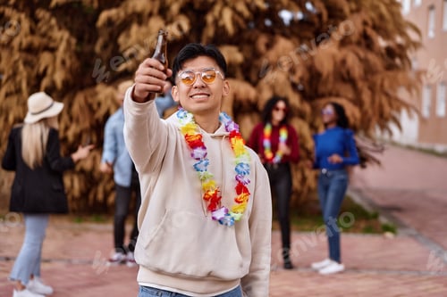 Preview: Happy man with a beer bottle partying with friends outdoors.