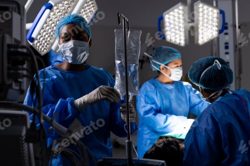 Preview: Diverse female doctors with face masks doing surgery in hospital operating room