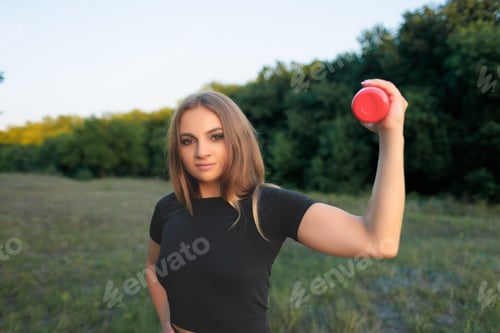 Preview: a young girl athlete holds a red bottle of water in her hand, showing her muscles on her arm