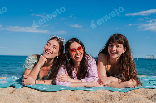 Preview: Group of only women lying down on the sand of the beach, smiling and looking at camera. Three young