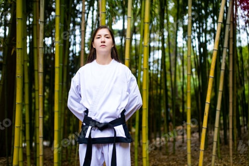 Preview: A young woman with a black belt coaches in martial art outdoor bamboo background