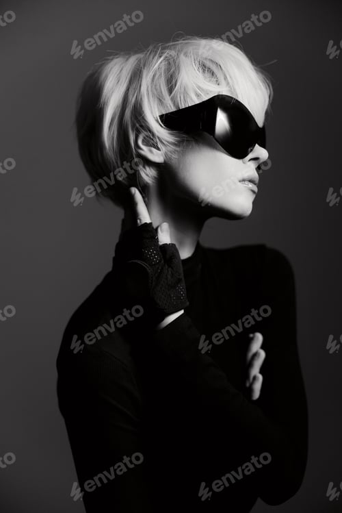 Preview: Stylish woman with short blonde hair wearing sunglasses, posing confidently against a dark