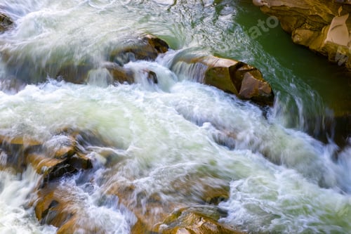Preview: Mountain river with small waterfall with clear turquoise water falling down between wet boulders