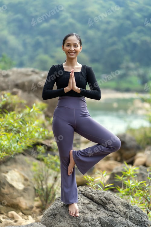Preview: Asian Indonesian Woman Practicing Yoga Alone in Nature on a Rock