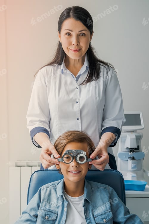 Preview: Cheerful middle aged ophthalmologist examining little boy with modern equipment